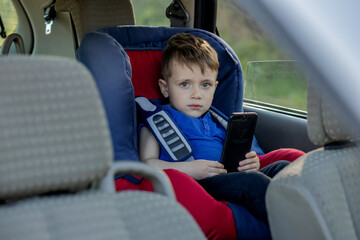 Portrait of a bored little boy sitting in a car seat. Safety of transportation of children.