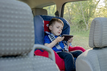 Portrait of a bored little boy sitting in a car seat. Safety of transportation of children.