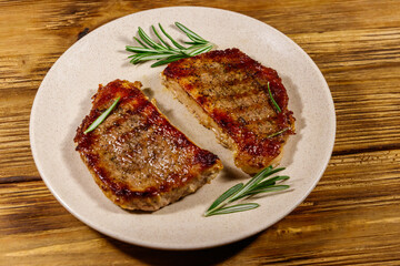Grilled pork steaks with rosemary on wooden table