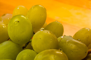 large brush of green grapes in a red ceramic plate on a wooden background