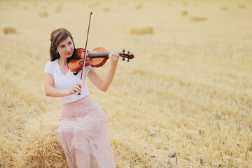 Beautiful romantic girl with loose hair playing the violin in the field.