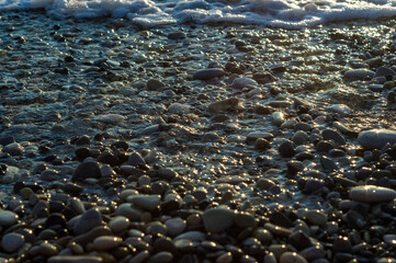 pebble stones on the sea beach, the rolling waves of the sea with foam