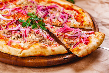Pizza with tuna and red onion on wooden cutting board. Close up