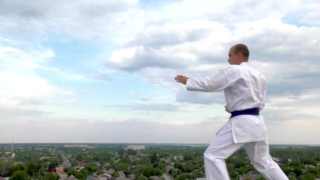 The athlete makes punches and kicks against the background of the sky with clouds