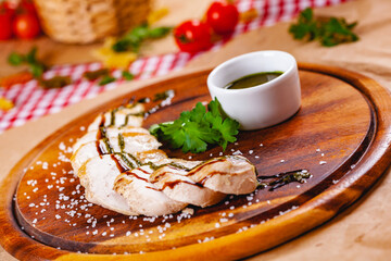 Sliced grilled chicken breast with pesto sauce on wooden cutting board. Close up
