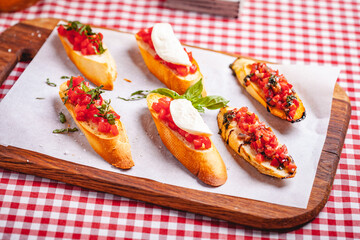 Traditional Italian bruschetta with cherry tomatoes, basil and mozzarella cheese on wooden cutting board. Close up