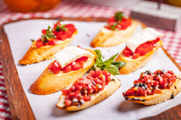 Traditional Italian bruschetta with cherry tomatoes, basil and mozzarella cheese on wooden cutting board. Close up