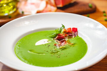Green pea cream soup with bacon in white plate. Close up
