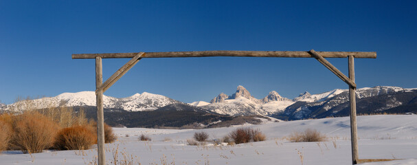 Panorama of Mount Owen Grand Middle and South Teton peaks in winter from an Idaho field with wood...