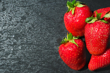 Fresh red strawberries with water drops on a black board. Copy space.