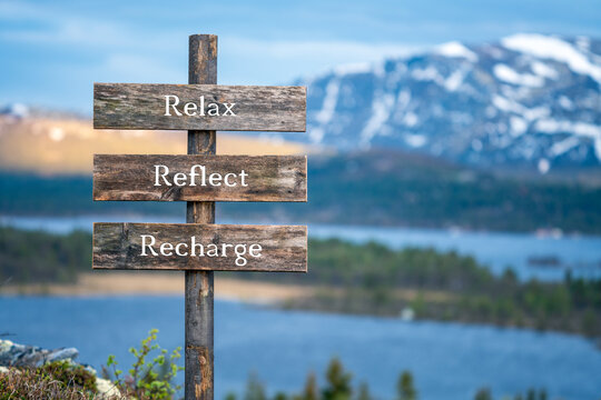 relax reflect recharge text on wooden signpost outdoors in landscape scenery during blue hour. Sunset light, lake and snow capped mountains in the back.