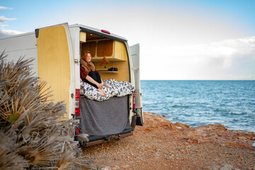 Thoughtful woman sitting in motor home at beach against sky