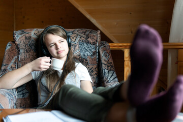 Obraz premium Dreaming teen girl sits with a cup in hand during break in school online webinar