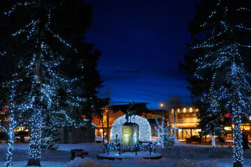 Fototapeta na wymiar Lights on Elk antler arches and trees in Jackson Wyoming town square in winter at twilight with cowboy on bucking broncho statue