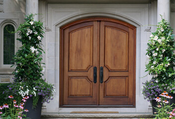 Elegant wooden double front door with curved top, surrounded by flowers