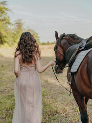 Obraz premium Young woman in a beige dress leads her horse along a road on a leash in.