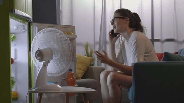 Woman talking on the phone at home and cooling in front of the fridge