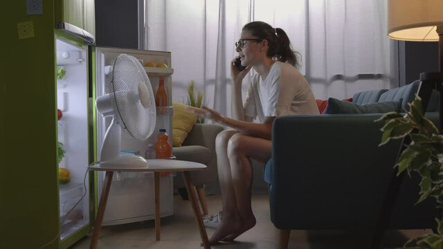 Woman talking on the phone at home and cooling in front of the fridge