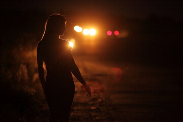 Silhouette of young slender woman in the backlight of car headlights on the road