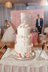 Wedding cake decorated with creamy roses at the background of the bride and groom