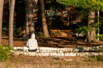 Person in gray hoodie sitting on a birch log facing the woods