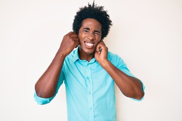 Handsome african american man with afro hair wearing casual clothes covering ears with fingers with annoyed expression for the noise of loud music. deaf concept.