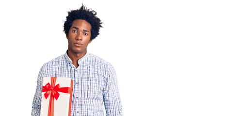Handsome african american man with afro hair holding gift thinking attitude and sober expression looking self confident