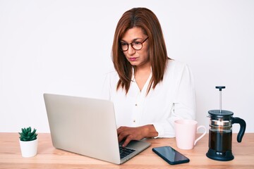 Middle age brunette hispanic business woman working at the office thinking attitude and sober expression looking self confident