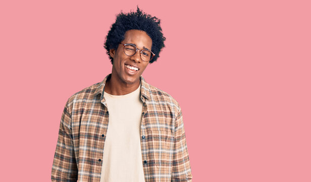 Handsome african american man with afro hair wearing casual clothes and glasses winking looking at the camera with sexy expression, cheerful and happy face.