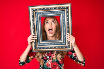 Young caucasian woman with blond hair holding empty frame angry and mad screaming frustrated and furious, shouting with anger looking up.