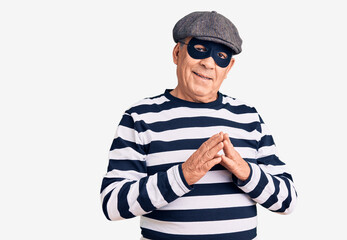 Senior handsome man wearing burglar mask and t-shirt hands together and fingers crossed smiling relaxed and cheerful. success and optimistic