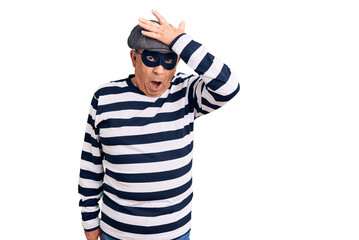 Senior handsome man wearing burglar mask and t-shirt surprised with hand on head for mistake, remember error. forgot, bad memory concept.