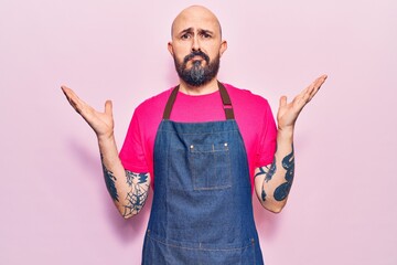 Young handsome man wearing apron clueless and confused with open arms, no idea and doubtful face.