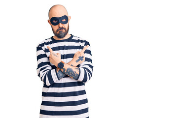 Young handsome man wearing burglar mask pointing to both sides with fingers, different direction disagree