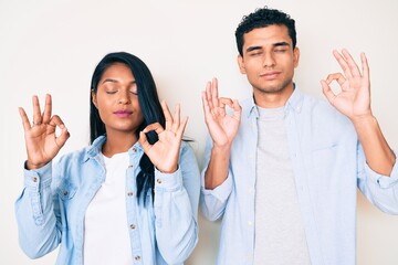 Beautiful latin young couple wearing casual clothes relax and smiling with eyes closed doing meditation gesture with fingers. yoga concept.