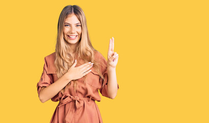 Beautiful caucasian woman with blonde hair wearing summer jumpsuit smiling swearing with hand on...