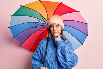 Young beautiful woman holding colorful umbrella serious face thinking about question with hand on chin, thoughtful about confusing idea