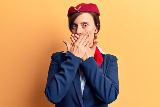 Young beautiful woman wearing stewardess uniform shocked covering mouth with hands for mistake. secret concept.