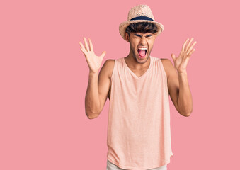 Young hispanic man wearing summer hat celebrating mad and crazy for success with arms raised and closed eyes screaming excited. winner concept