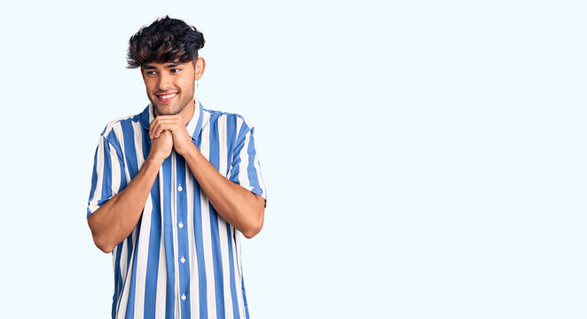 Young hispanic man wearing casual clothes laughing nervous and excited with hands on chin looking to the side