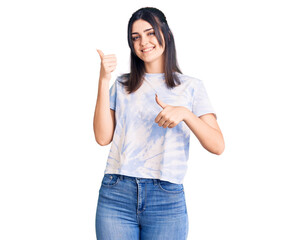 Obraz na płótnie Canvas Young beautiful girl wearing casual t shirt pointing to the back behind with hand and thumbs up, smiling confident
