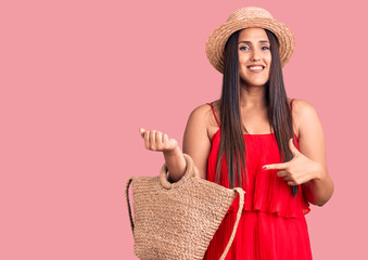 Young beautiful brunette woman wearing summer hat and dress holding bag smiling happy pointing with hand and finger