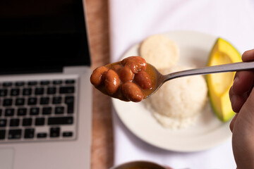 Frijoles en mesa de trabajo en casa para almorzar con arroz arepa y aguacate. Plato tradicional para comer mientras trabajamos en casa cuchara a punto de comer frijoles rojos