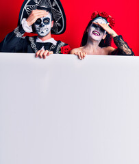 Young couple wearing mexican day of the dead costume holding blank empty banner stressed and frustrated with hand on head, surprised and angry face