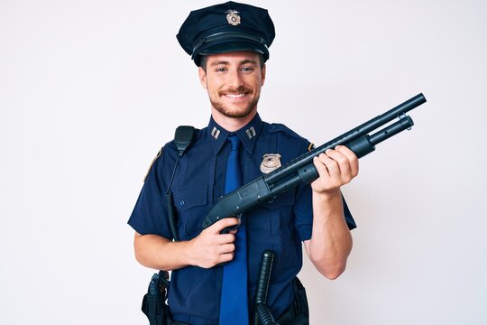 Young caucasian man wearing police uniform holding shotgun smiling with a happy and cool smile on face. showing teeth.