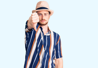 Young handsome caucasian man wearing summer hat looking unhappy and angry showing rejection and negative with thumbs down gesture. bad expression.