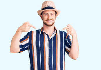 Naklejka premium Young handsome caucasian man wearing summer hat looking confident with smile on face, pointing oneself with fingers proud and happy.