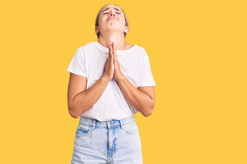 Young beautiful blonde woman wearing casual white tshirt begging and praying with hands together with hope expression on face very emotional and worried. begging.