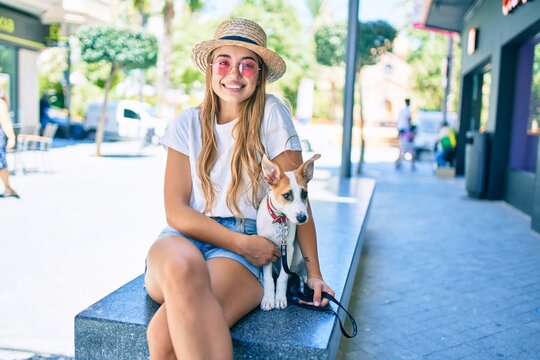 Young beautiful blonde woman walking the dog outside on a summer day sitting on a bench