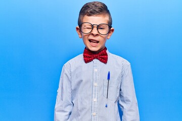 Cute blond kid wearing nerd bow tie and glasses winking looking at the camera with sexy expression, cheerful and happy face.